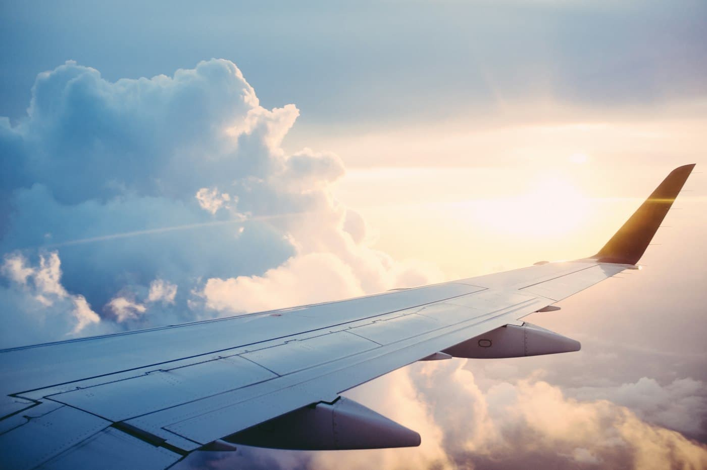 Airplane wing above clouds — travel is part of the decision, not a holiday package.